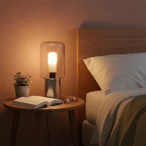 A bedside table with a stylish lamp, an open book, and glasses, creating a cozy reading atmosphere.
