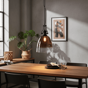 Black metal pendant light with faded rose gold glass shade hanging over a wooden dining table.