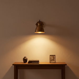 Antique brass wall lamp illuminating a wooden table with a vase, books, and a framed picture.