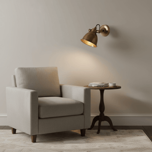 Antique brass wall lamp mounted above a cozy armchair and side table, providing warm ambient light.