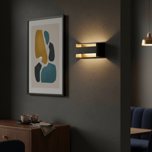 Feloniche LED Wall Light in black and gold illuminating a wall beside framed artwork, creating a warm ambiance.