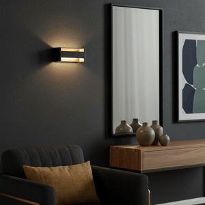 Black and gold LED wall light illuminating a dark wall beside a mirror and decorative vases.