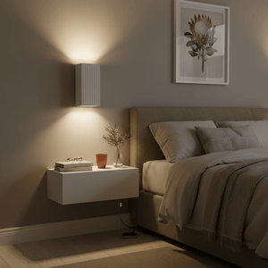 Clara Up & Down Wall Light in a cozy bedroom setting, illuminating the wall above a bedside table.