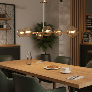Horizontal pendant light with amber glass shades above a wooden dining table set with a croissant and coffee.