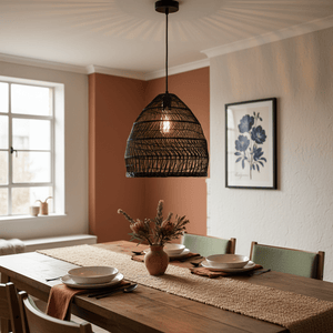 Black rattan pendant light hanging above a wooden dining table set with plates and a vase of flowers.