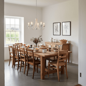 White 5-light chandelier hanging over a wooden dining table set for breakfast in a bright room.