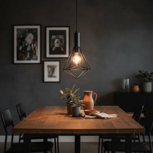 Black metal pendant light with geometric design hanging above a wooden dining table, surrounded by plants and decor.