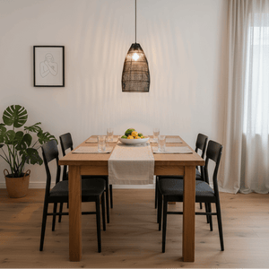 Black rattan pendant light hanging above a wooden dining table set with glasses and a fruit bowl.