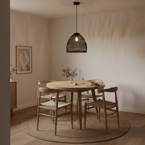 Black rattan pendant light hanging above a wooden dining table set with dishes and a vase.