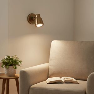 Antique brass Indigo Swirl wall lamp mounted beside a cozy armchair with a plant and an open book.