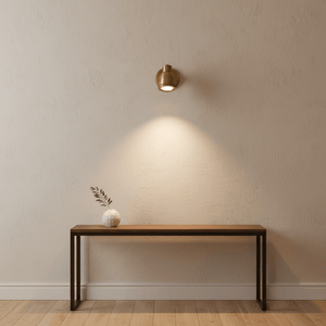 Antique brass Indigo Swirl wall lamp mounted on a textured wall, illuminating a wooden console table with a decorative vase.