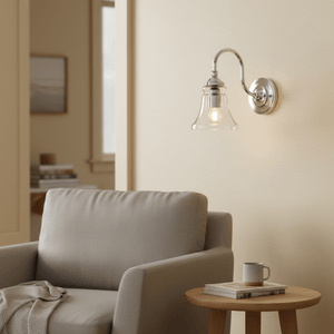 Antique silver wall lamp with clear glass diffuser mounted beside a cozy armchair and side table.