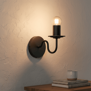 Harry Black Indoor Wall Light mounted on a textured wall, illuminating a wooden table with books and a cup.