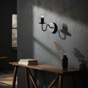 Harry Black Indoor Wall Light mounted on a textured wall, casting shadows, with a wooden table and decorative vase.