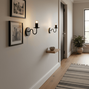 Two Harry Black Indoor Wall Lights mounted on a wall, illuminating framed photos in a cozy hallway.