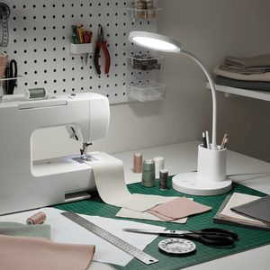 Dimmable rechargeable LED desk lamp illuminating a sewing area with fabric and tools.
