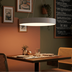 Modern LED pendant light hanging above a dining table set with plates and glasses, surrounded by framed artwork.