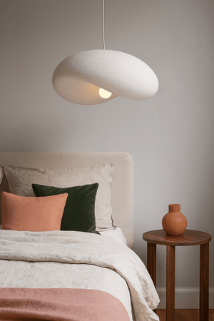 Ivory Drift 500 Pendant Light hanging above a bed with decorative pillows and a wooden side table.