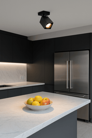 Square matt black spotlight mounted on ceiling illuminating a bowl of colorful fruit on a marble countertop.