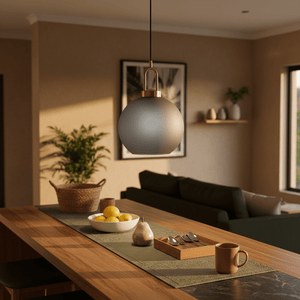Smoke-grey pendant light with antique brass detailing hanging above a wooden dining table set with fruit and utensils.