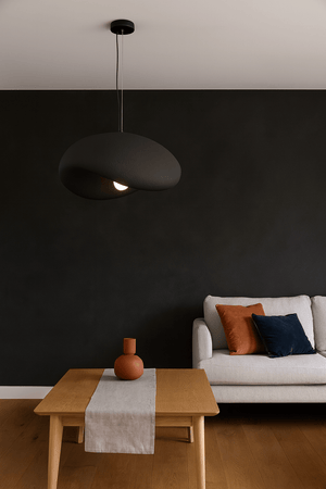 Obsidian Drift 700 Pendant Light hanging above a wooden table with decorative items and a sofa in a modern interior.