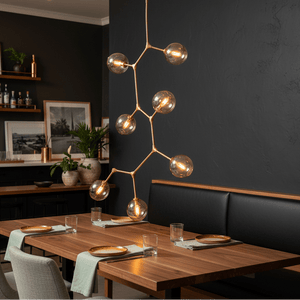 Vertical 7-light pendant in gold above a wooden dining table with plates and glasses.
