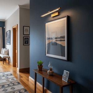 Antique bronze picture light mounted above a framed artwork in a stylish hallway setting.