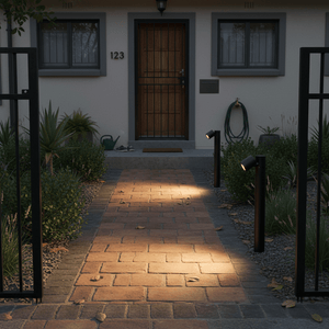 Two black bollard lights illuminate a brick pathway leading to a front door.