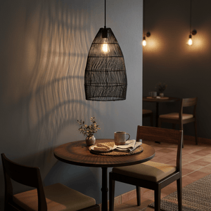 Black rattan pendant light hanging above a small dining table with a plant and tableware.