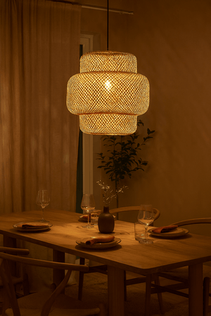 Bamboo rattan pendant light hanging over a wooden dining table set for a meal, creating a warm ambiance.