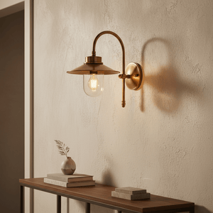 Antique brass wall lamp with clear glass diffuser mounted on a textured wall, casting soft shadows.