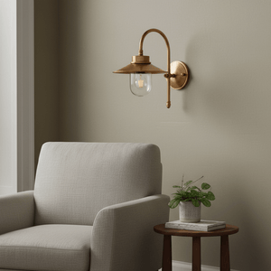 Antique brass wall lamp with clear glass diffuser mounted beside a cozy armchair and plant.