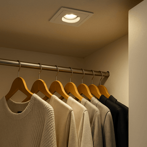 LED cabinet light installed in a closet ceiling, illuminating hanging clothes with warm white light.