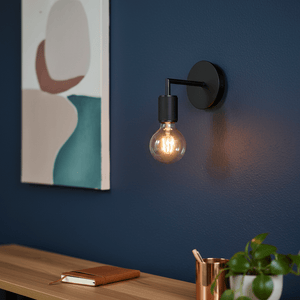 Black wall light mounted on a blue wall, illuminating a stylish interior with a painting and wooden shelf.