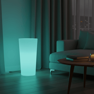 A glowing RGBW planter lamp beside a modern couch, casting a soft teal light in a cozy living room.