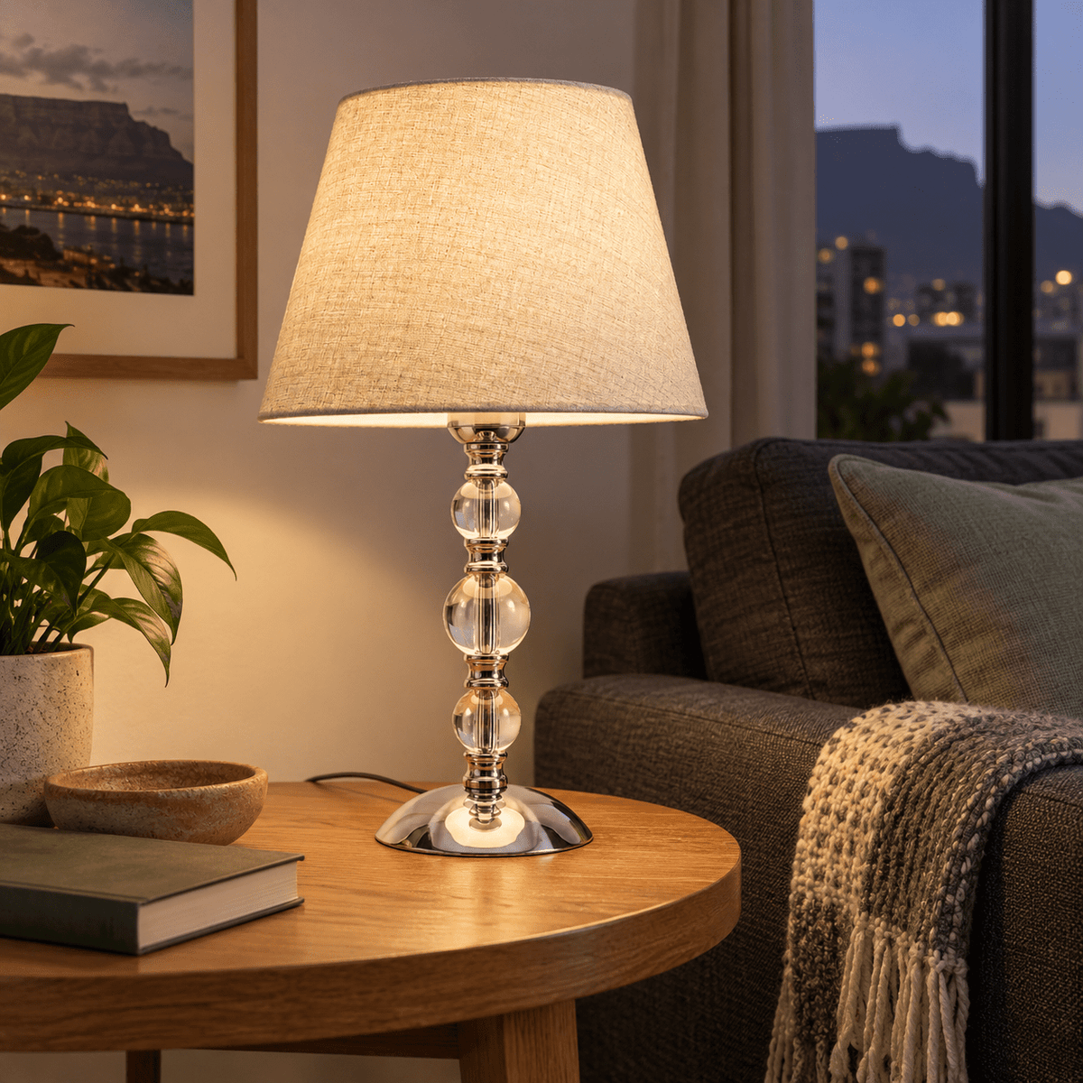 Myrna Satin Chrome Table Lamp with Hessian Shade — on an oak side table beside a charcoal sofa