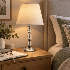 Myrna Satin Chrome Table Lamp with Hessian Shade — beside a bed with sage linens