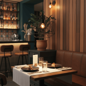 Black metal pendant light illuminating a dining table set with plates and glasses in a cozy restaurant.
