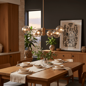 Stylish dining setup featuring a gold and amber glass pendant light above a wooden table with plates and greenery.