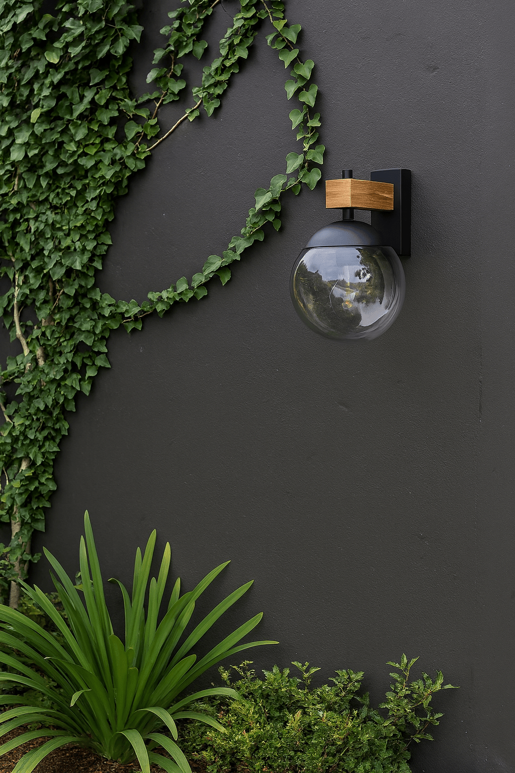 Bufalata Outdoor Wall Light mounted on a dark wall, surrounded by lush green plants.