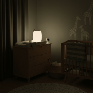 A softly glowing Bon Bon bedside night light on a dresser beside a crib, creating a calming atmosphere.