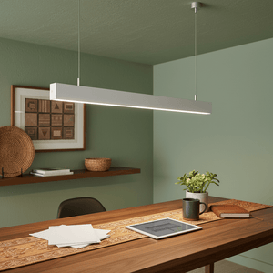 Suspended linear pendant light above a wooden table with a plant, tablet, and decorative items.