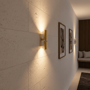 Banyan Gold Up & Down Wall Light illuminating a textured wall, flanked by framed artwork in a modern setting.