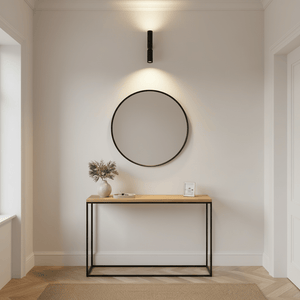 Modern black up and down wall light above a wooden console table with a round mirror and decorative vase.