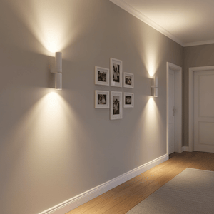 Banyan White Up & Down Wall Light illuminating a hallway with framed photos on the wall.