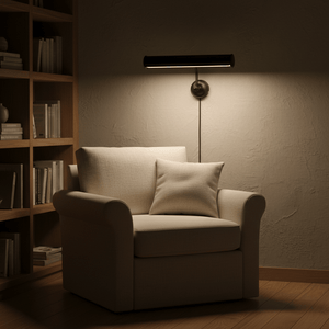 Matt black wall lamp illuminating a cozy armchair with a pillow, set against a bookshelf backdrop.