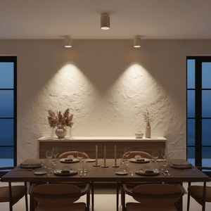 Cove Travertine Marble Downlight Holder mounted on a textured wall, illuminating a dining table set with dishes and glassware.