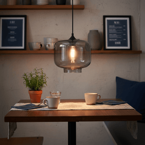 Smoke grey Elza glass pendant light hanging above a dining table set with cups and a plant.