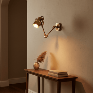 Antique brass swing wall lamp illuminating a wooden table with books and a vase.