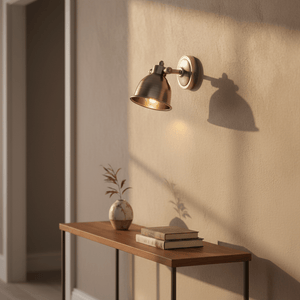 Antique silver wall lamp illuminating a wooden table with books and a vase, casting soft shadows.